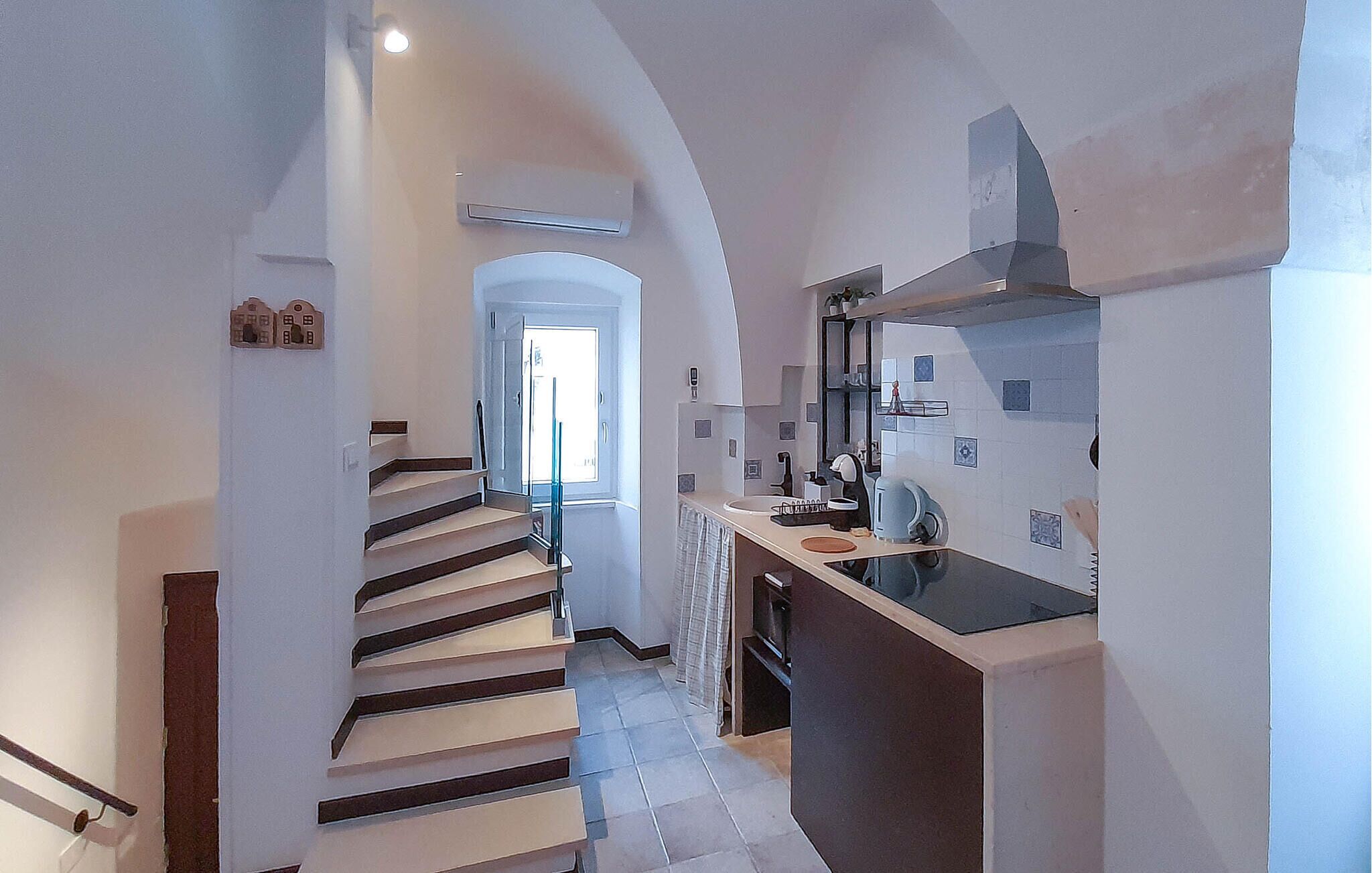 Ein schmaler Flur, der zu einer Treppe und einem modernen Küchenbereich mit einer großen Kochinsel und einem eingebauten Backofen führt.