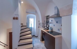 Ein schmaler Flur, der zu einer Treppe und einem modernen Küchenbereich mit einer großen Kochinsel und einem eingebauten Backofen führt.