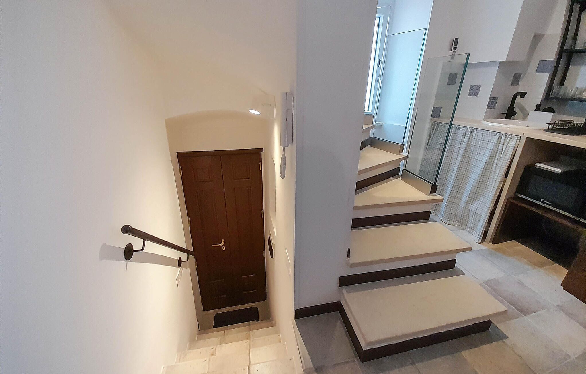 A staircase leading to a landing with a door, a kitchen area with a sink and cabinets, and a window providing natural light.