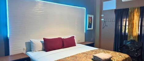 A hotel room with a bed, bedside table, lamp, and a view of the outside.