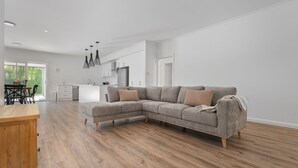 Ein modernes Wohnzimmer mit Ecksofa, Holzboden und Essbereich mit Holztisch.