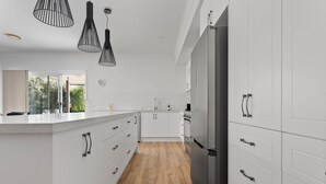 Eine moderne Küche mit weißen Schränken, einem Edelstahl-Kühlschrank und schwarzen Pendelleuchten.