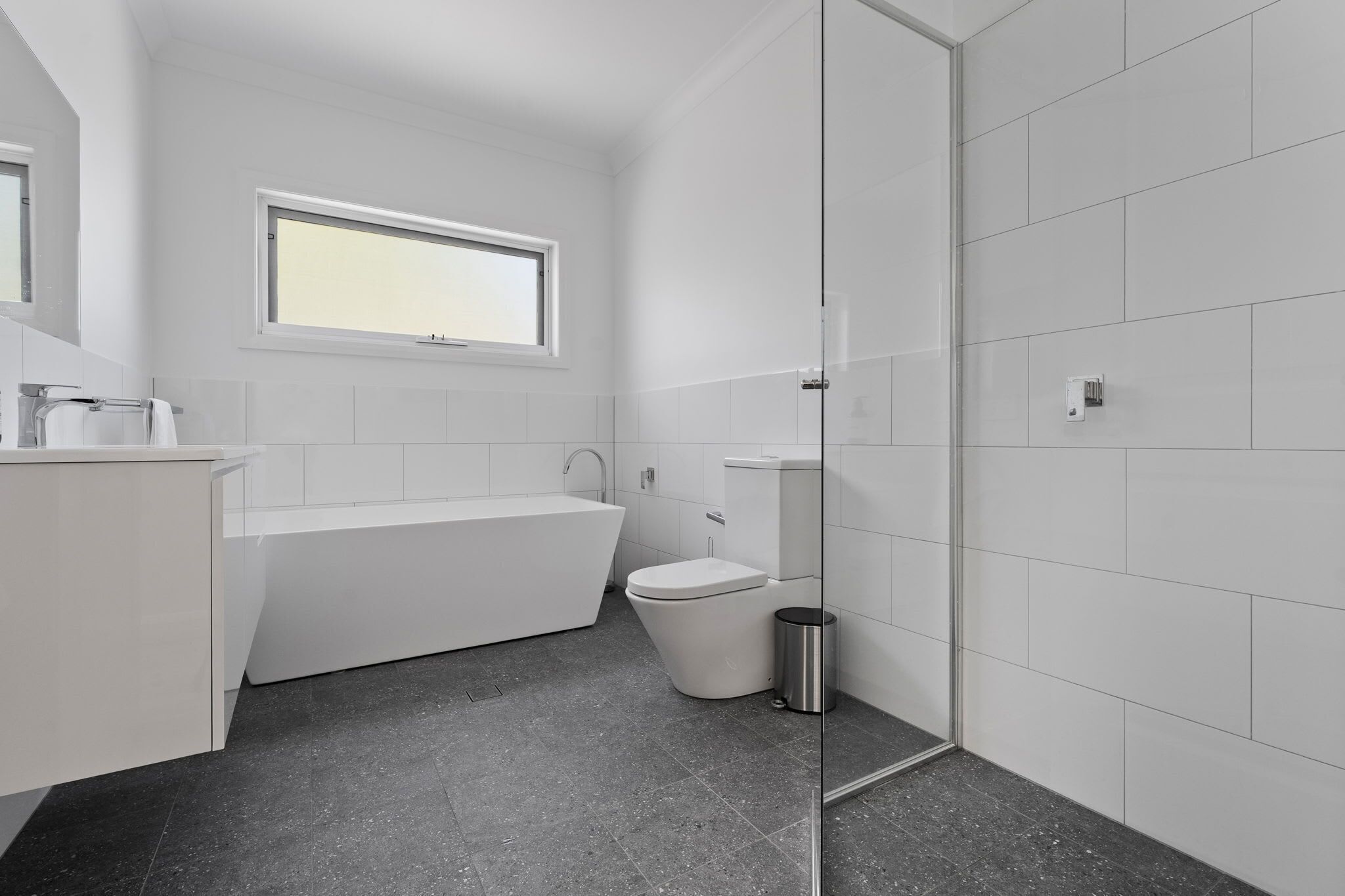 A modern bathroom with a bathtub, toilet, and a window.