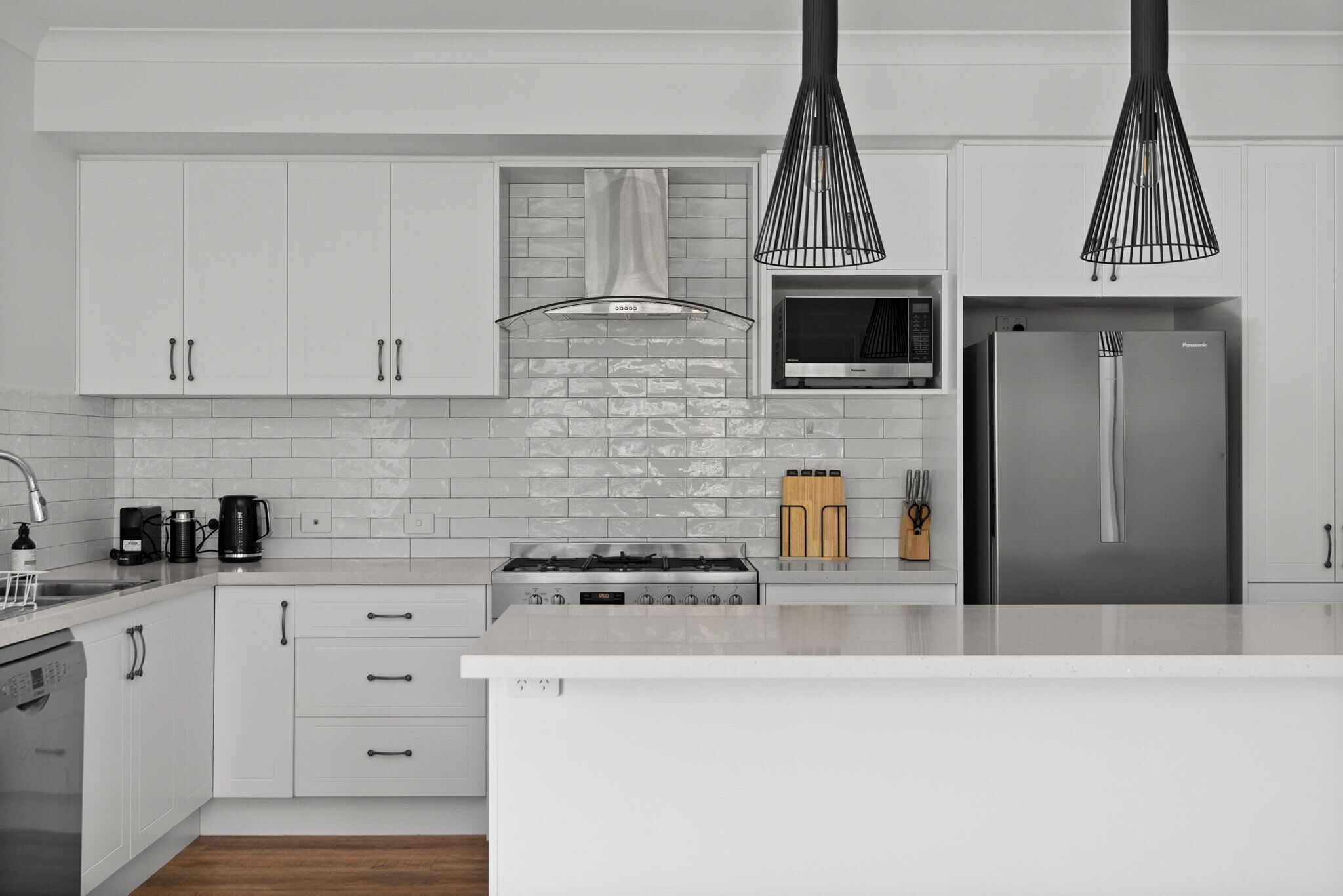 Una cocina moderna con armarios blancos, un refrigerador de acero inoxidable, una estufa a gas e iluminación colgante.