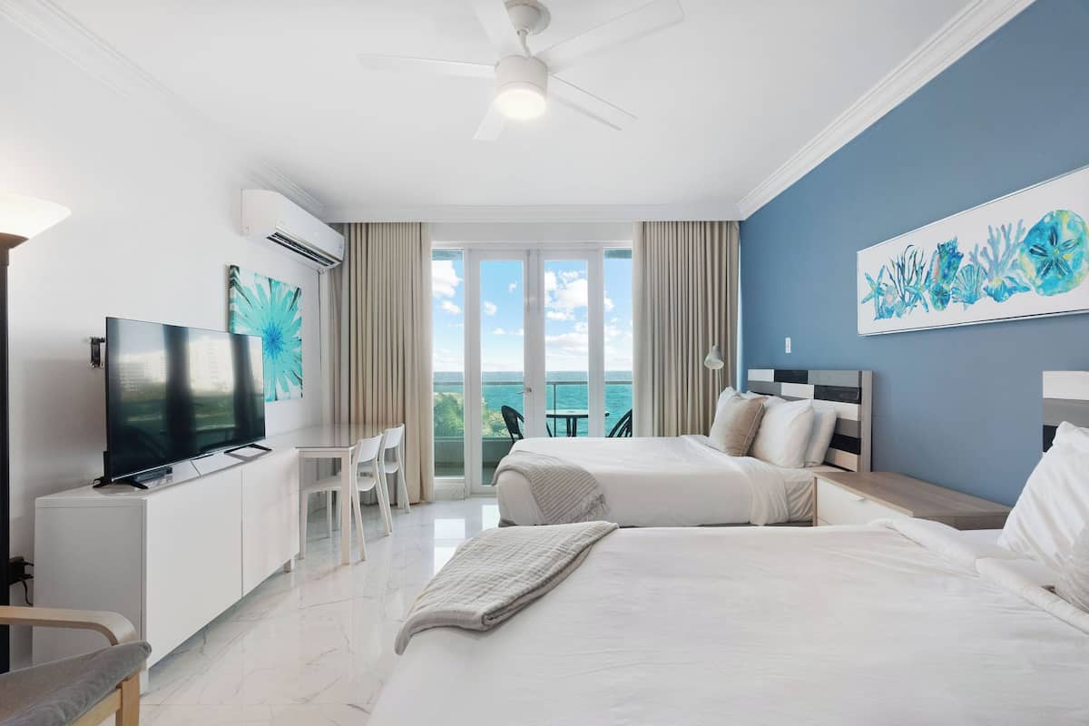 Habitación de hotel con cama, televisión, escritorio, silla y balcón con vistas.