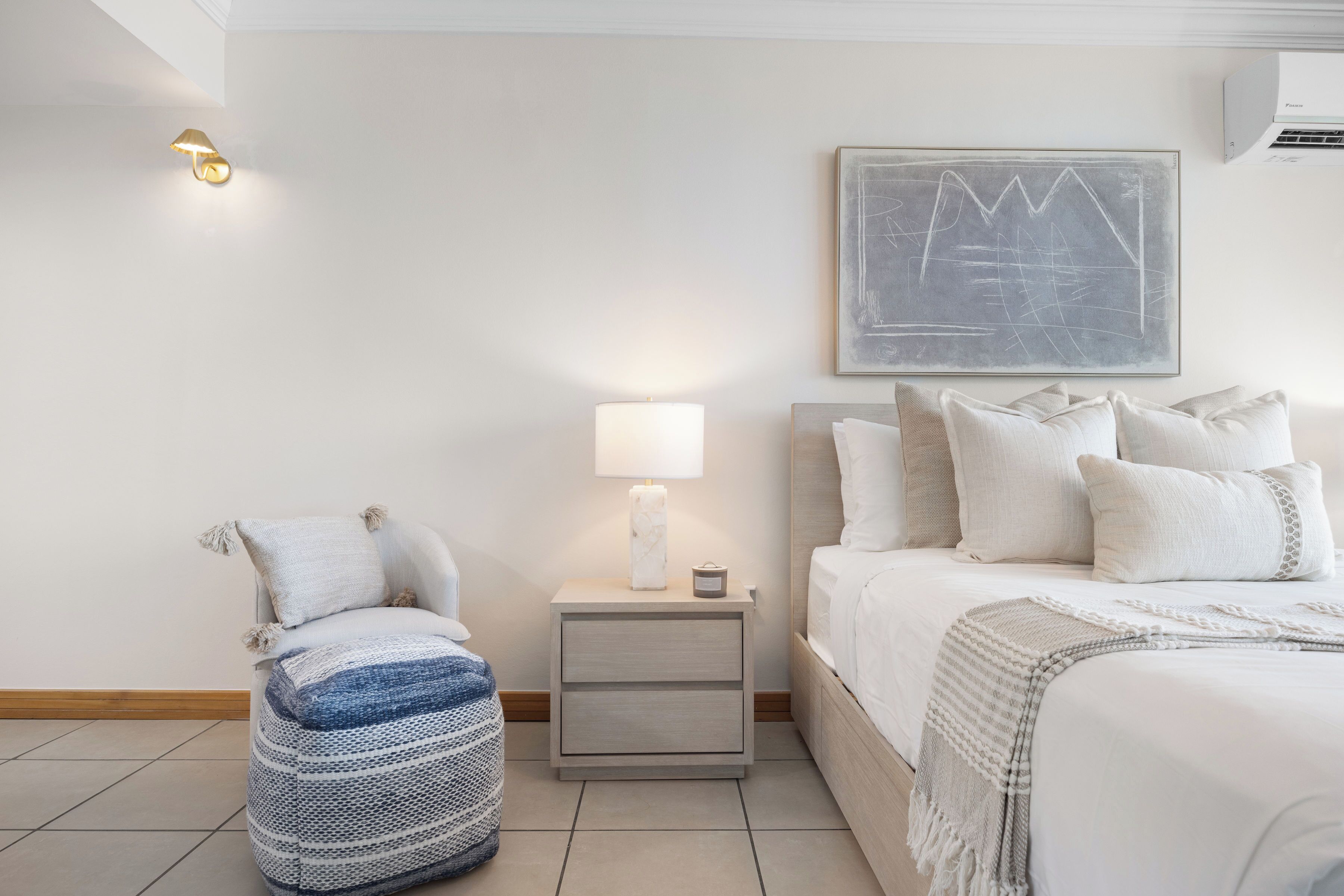 Quarto com cama, luminária de cabeceira, mesa de apoio e uma obra de arte na parede.