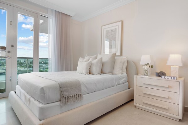 A bedroom with a bed, a nightstand, a framed picture, and a view through a glass door. - Condado Lagoon - Lux Waterfront Studios (San Juan)