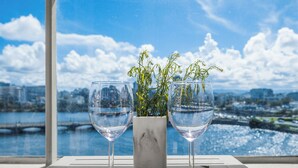 Two wine glasses on a table with a view of a cityscape and a body of water.