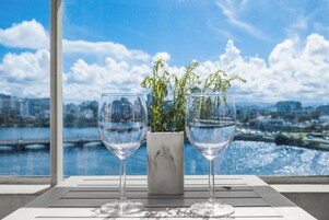 Dos copas de vino sobre una mesa con vistas a un paisaje urbano y una masa de agua.