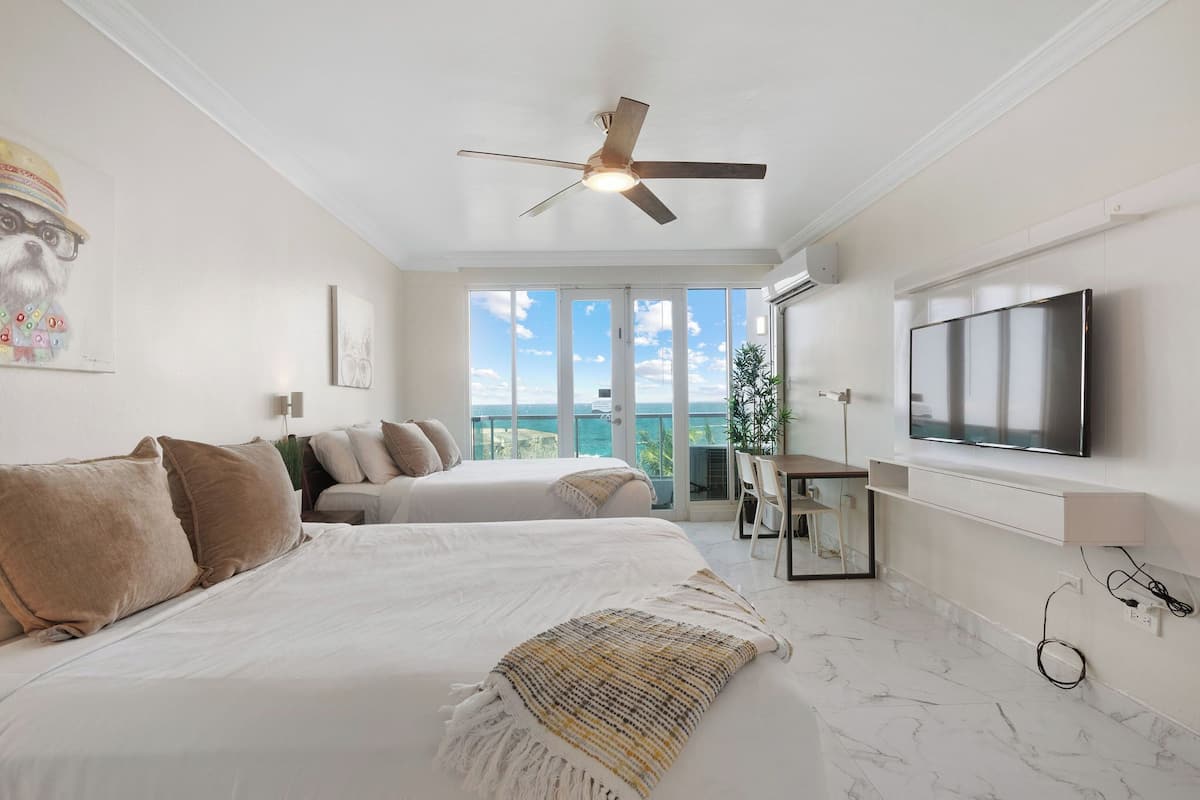 Una habitación de hotel con cama, ventilador de techo, televisor y balcón con vistas.