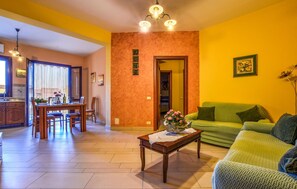 A living room with a green sofa, a wooden coffee table with a vase, a dining area with a table and chairs, and a kitchen visible through an open door. - Cozy apartment in Trappeto with WiFi (Trappeto)
