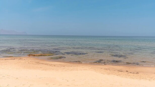 Una playa con aguas cristalinas, una orilla arenosa y montañas a lo lejos.