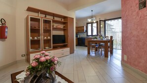 Una sala de estar con televisor, armarios de madera y un comedor con sillas y una mesa.