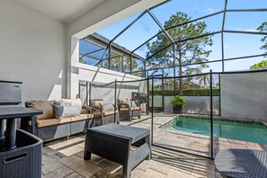 A covered outdoor patio with wicker furniture, a pool, and a view of trees. - Stylish Pool Home Near Disney | BBQ + Spacious Retreat for 10 (Clermont)