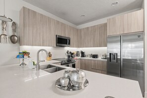 A modern kitchen with stainless steel appliances, a microwave, and a refrigerator. - Stylish Pool Home Near Disney | BBQ + Spacious Retreat for 10 (Clermont)