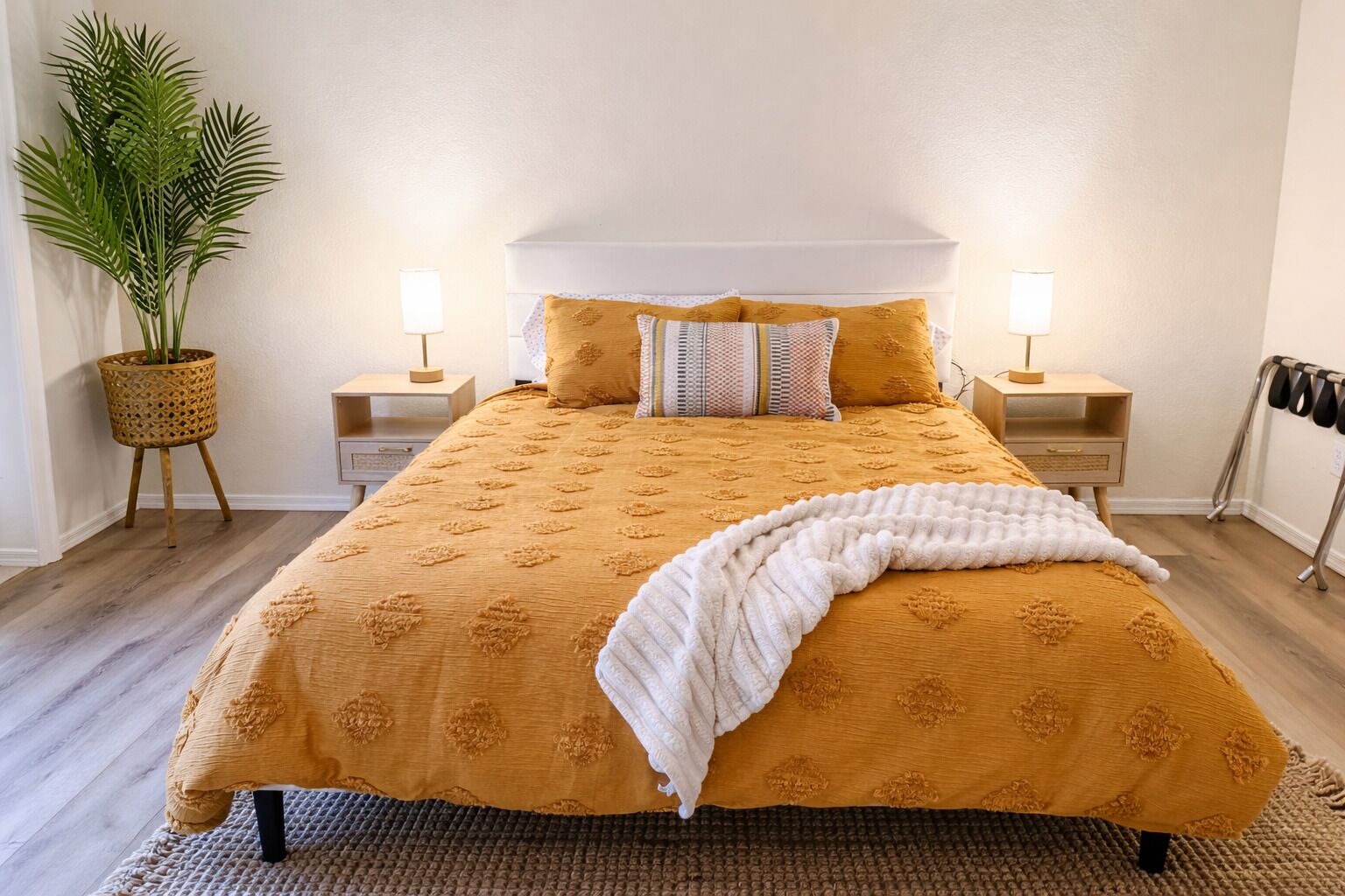 Una cama con una colcha estampada, dos lámparas de noche, una planta en maceta y una mesita de noche.