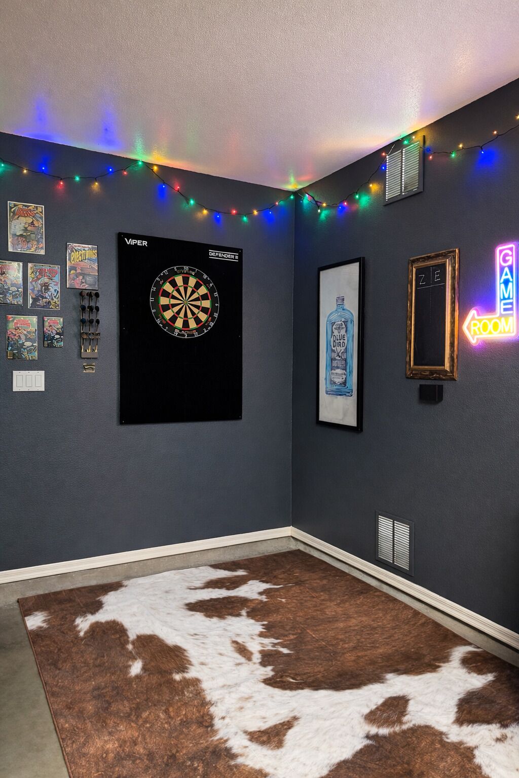 A room with a dartboard, framed comics, string lights, a cowhide rug, and a neon sign.