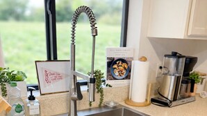 Eine moderne Küche mit einer Edelstahl-Spüle, einer Kaffeemaschine und einem gerahmten Zitat an der Wand.
