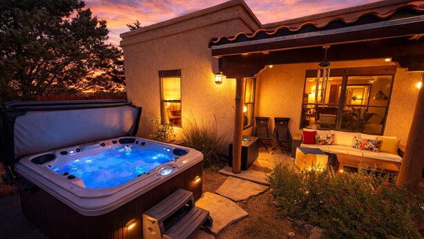 Ein Whirlpool mit einer Holzbank, ein überdachter Sitzbereich mit Tisch und eine Terrasse mit Pflanzen.