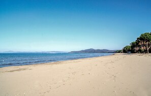 Una playa con cielos despejados, agua tranquila y montañas al fondo.