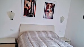 Een slaapkamer met een bed, een nachtkastje, een wandlamp en twee ingelijste foto's.