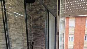 Een moderne badkamer met een douchecabine van glas, een houten bankje en een rode mat.