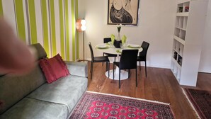 Een eetgedeelte met een ronde tafel, zwarte stoelen, een kamerkleed met patroon, een bank met een rood kussen en een gestreepte wand.