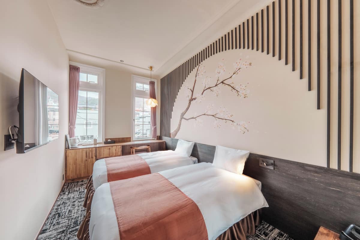 A hotel room with two beds, a wooden desk, a mirror, and a wall-mounted artwork.