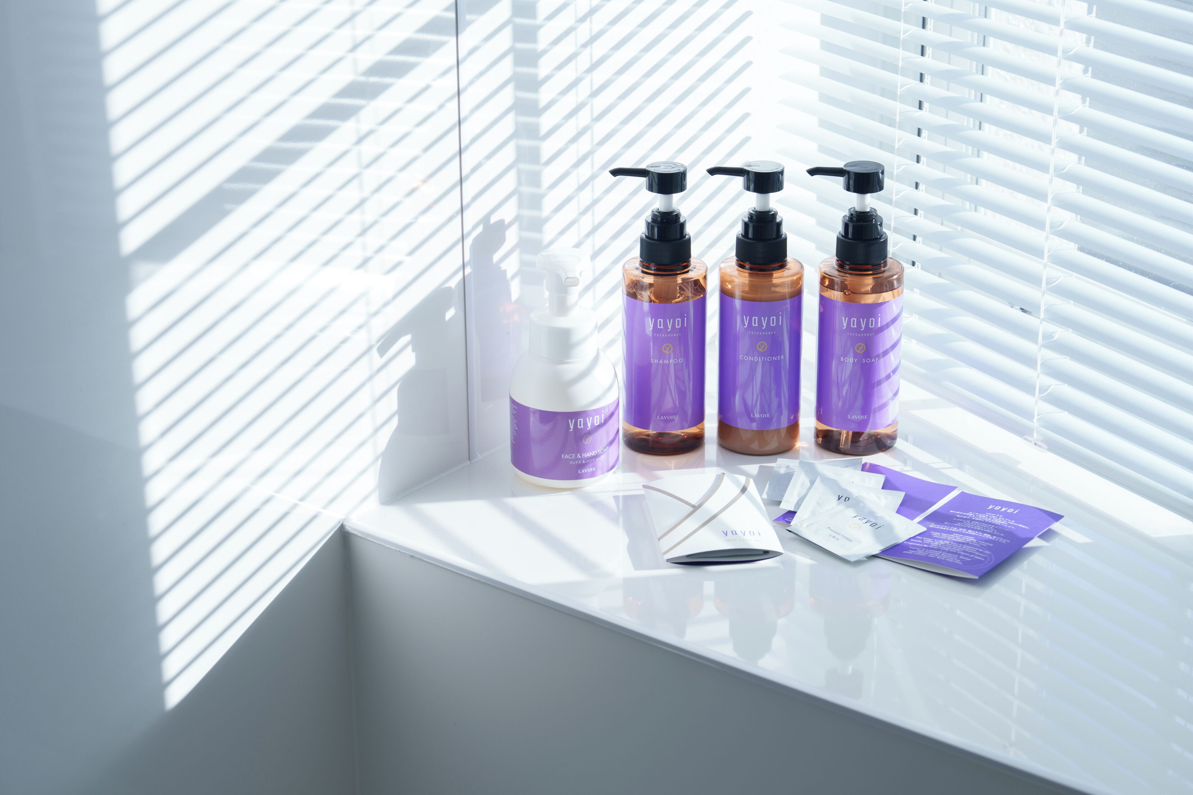 A bathroom with a window, white sink, and three bottles of shampoo and conditioner.