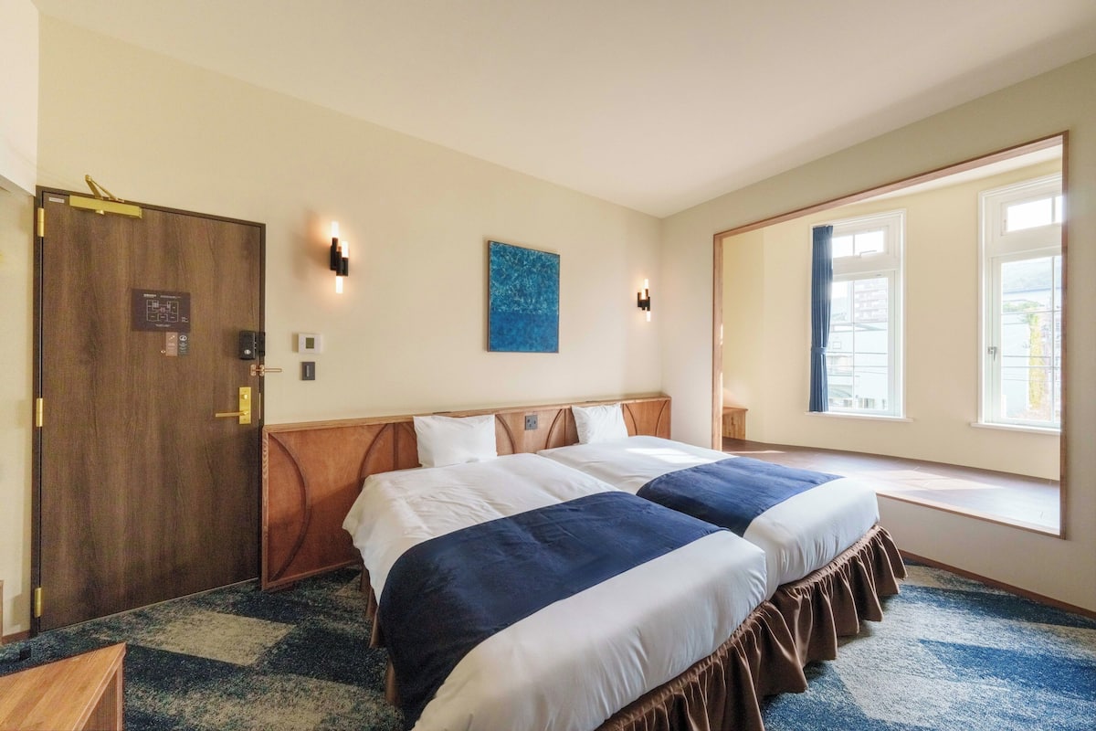 A hotel room with two beds, a large mirror, a window with a view, and a door with a digital lock.