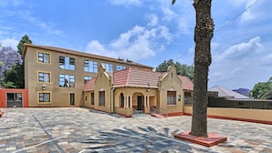 A building with multiple windows, a tiled courtyard, and a palm tree. - Room-45 On Westmoreland Luxury Guest Hou (Johannesburg)