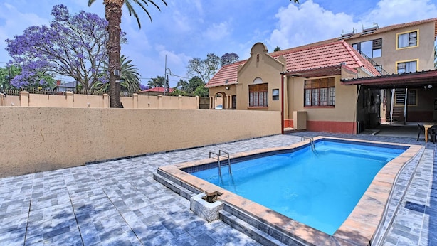 A swimming pool with a tiled deck, a palm tree, and a building with a red-tiled roof. - Room-45 On Westmoreland Luxury Guest Hou (Johannesburg)