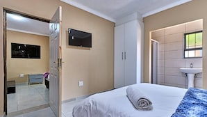 A bedroom with a bed, a TV mounted on the wall, a wardrobe, and a bathroom with a sink. - Room-45 On Westmoreland Luxury Guest Hou (Johannesburg)