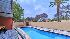 A swimming pool with a tiled deck, a wooden bench, and a palm tree. - Room-45 On Westmoreland Luxury Guest Hou (Johannesburg)