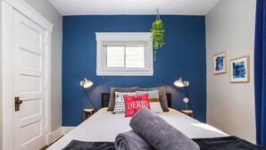 Ein Schlafzimmer mit einem Bett, Nachttischlampen, einem Fenster und einer hängenden Pflanze.