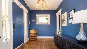 Ein Flur mit Holzboden, blauer Wand, weißer Tür, Fenster mit hängender Pflanze und einem schwarzen Konsolentisch mit einer Vase.