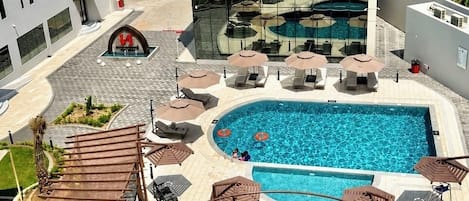 A rooftop pool area with lounge chairs, umbrellas, and a view of the mountains.