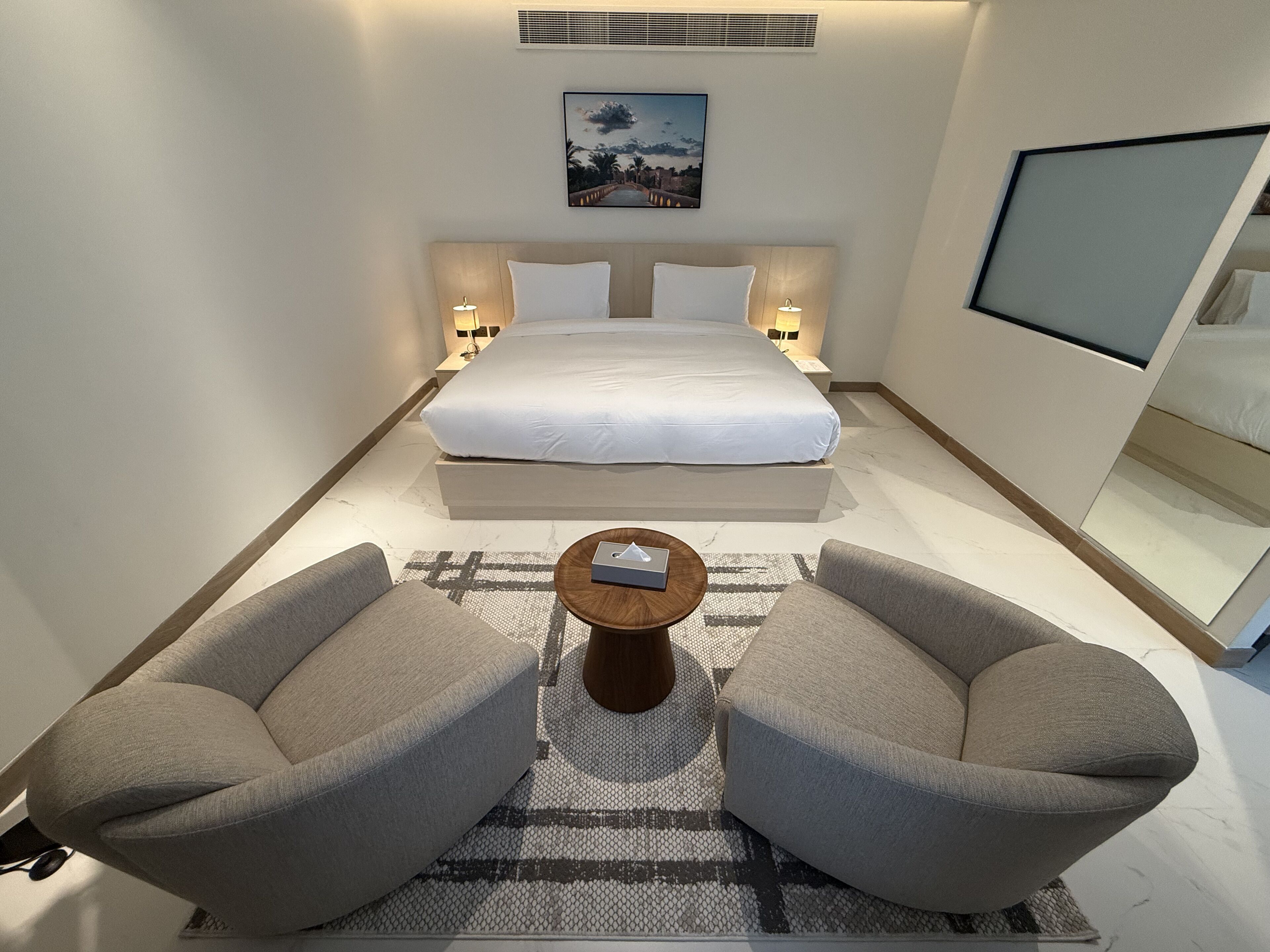 Een hotelkamer met een bed, twee fauteuils, een salontafel, een televisie en een schilderij aan de muur.