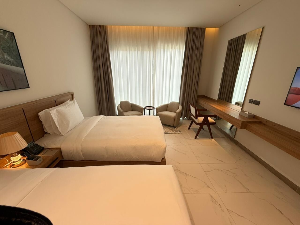 A hotel room with two beds, a desk, a chair, and a large mirror.
