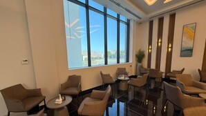 Un vestíbulo de hotel con diseño moderno, que cuenta con un amplio ventanal con vistas a la ciudad, varias zonas de estar y un suelo pulido.