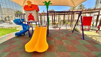 Un terrain de jeux avec des toboggans et des balançoires, installé sous une sorte de tonnelle ou de pergola.