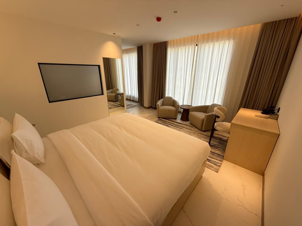 A hotel room with a large bed, a desk, a chair, and a television.