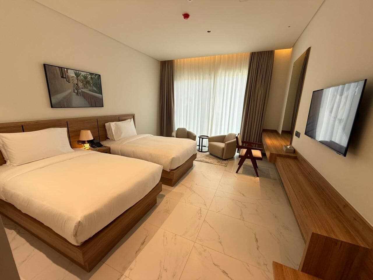 Ein Hotelzimmer mit zwei Betten, einem Fernseher, einem Schreibtisch, einem Stuhl und einem fenster mit Vorhängen.