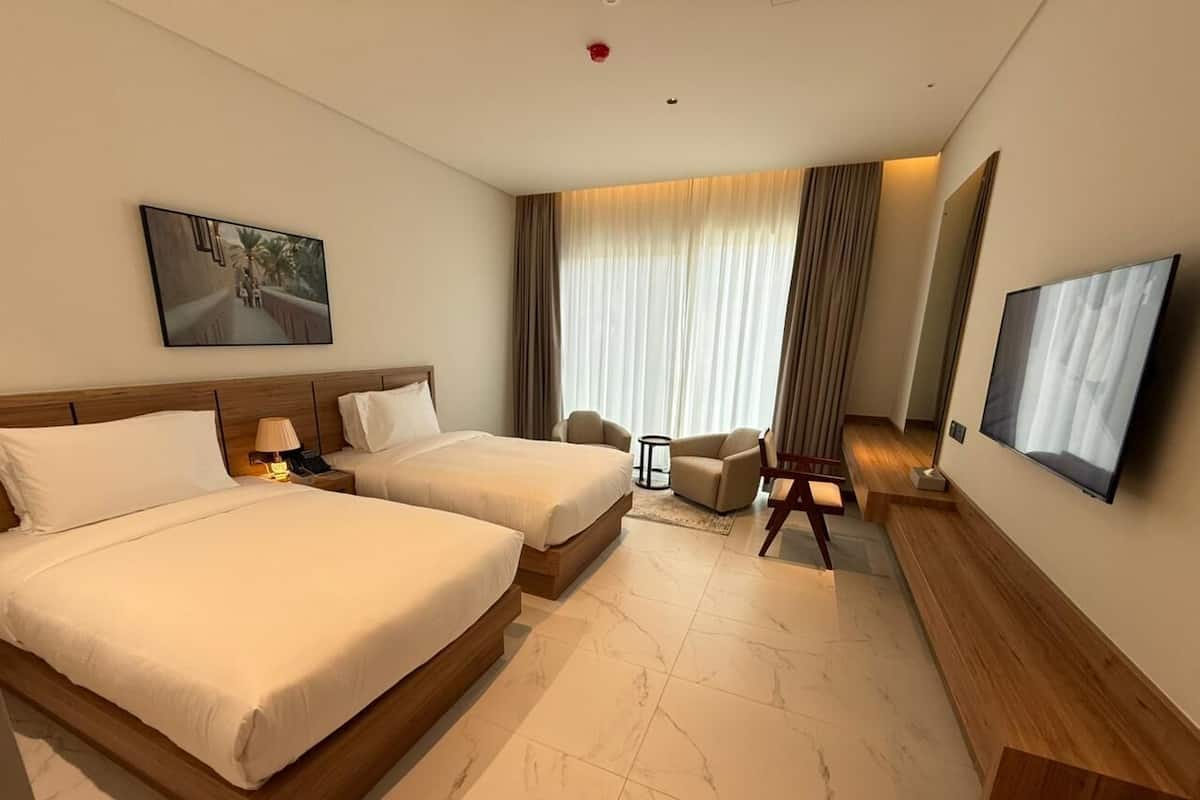 A hotel room with two beds, a TV, a desk, a chair, and a window with curtains.