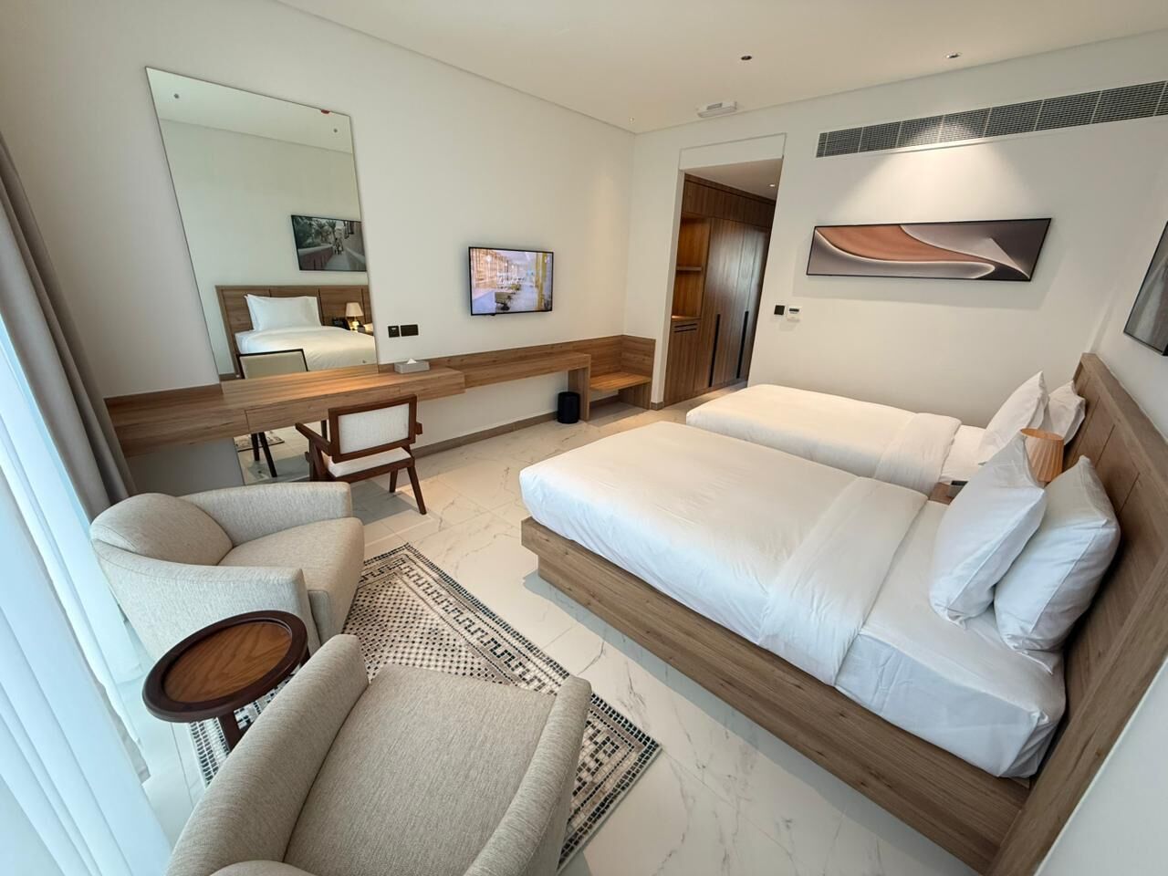 Ett hotellrum med en stor säng, en sittgrupp med en stol och ett bord, en TV och en spegel.