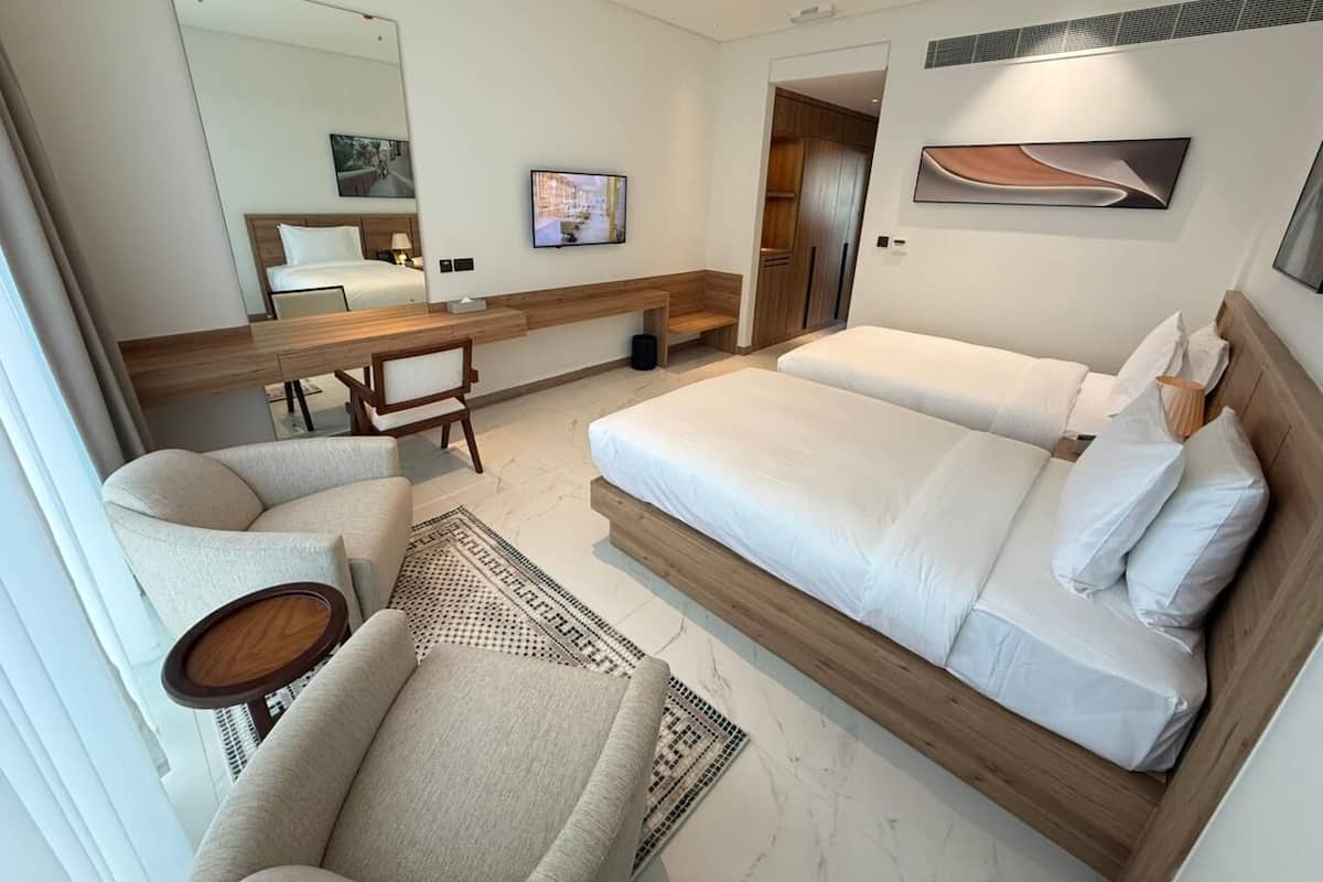 A hotel room with a large bed, a seating area with a chair and table, a TV, and a mirror.
