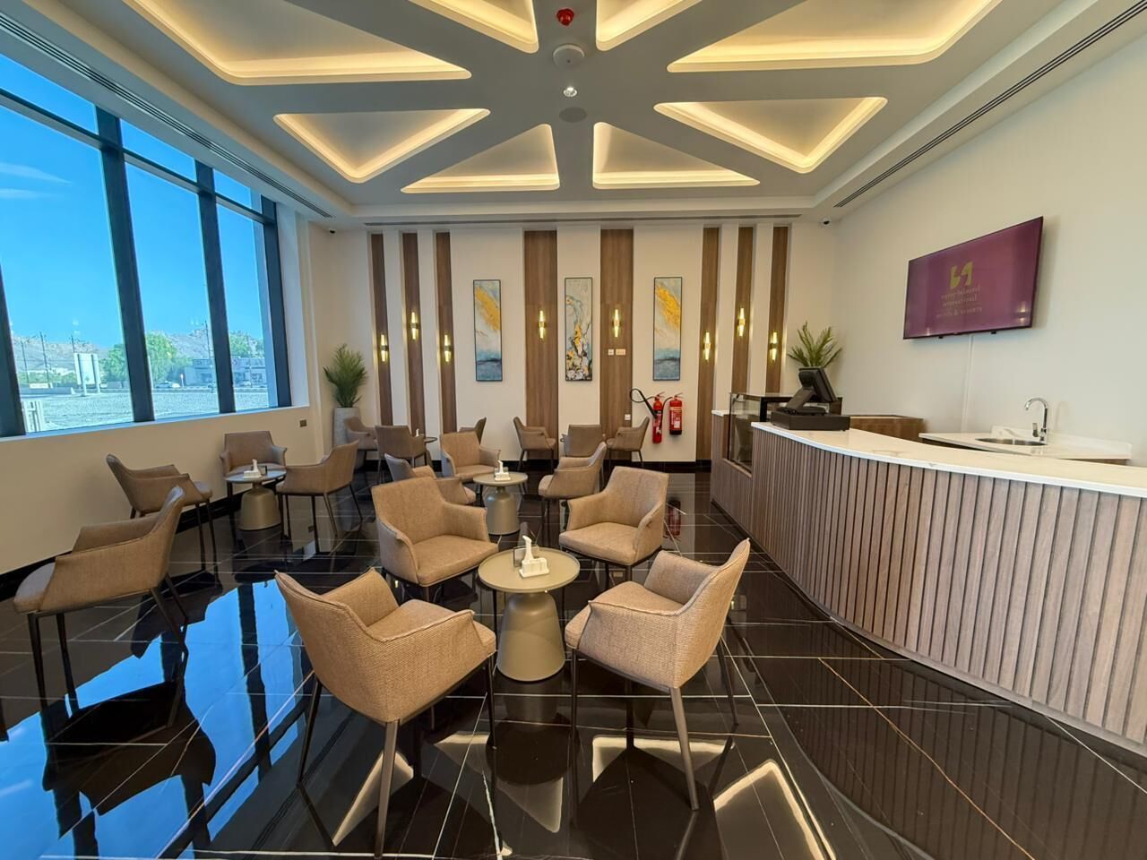 A modern hotel lobby with a reception desk, seating area, and large windows.