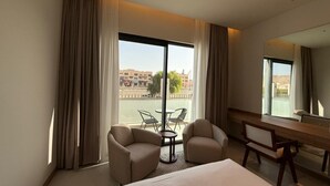 Habitación de hotel con cama, dos sillones, una mesita, escritorio y un ventanal con cortinas.