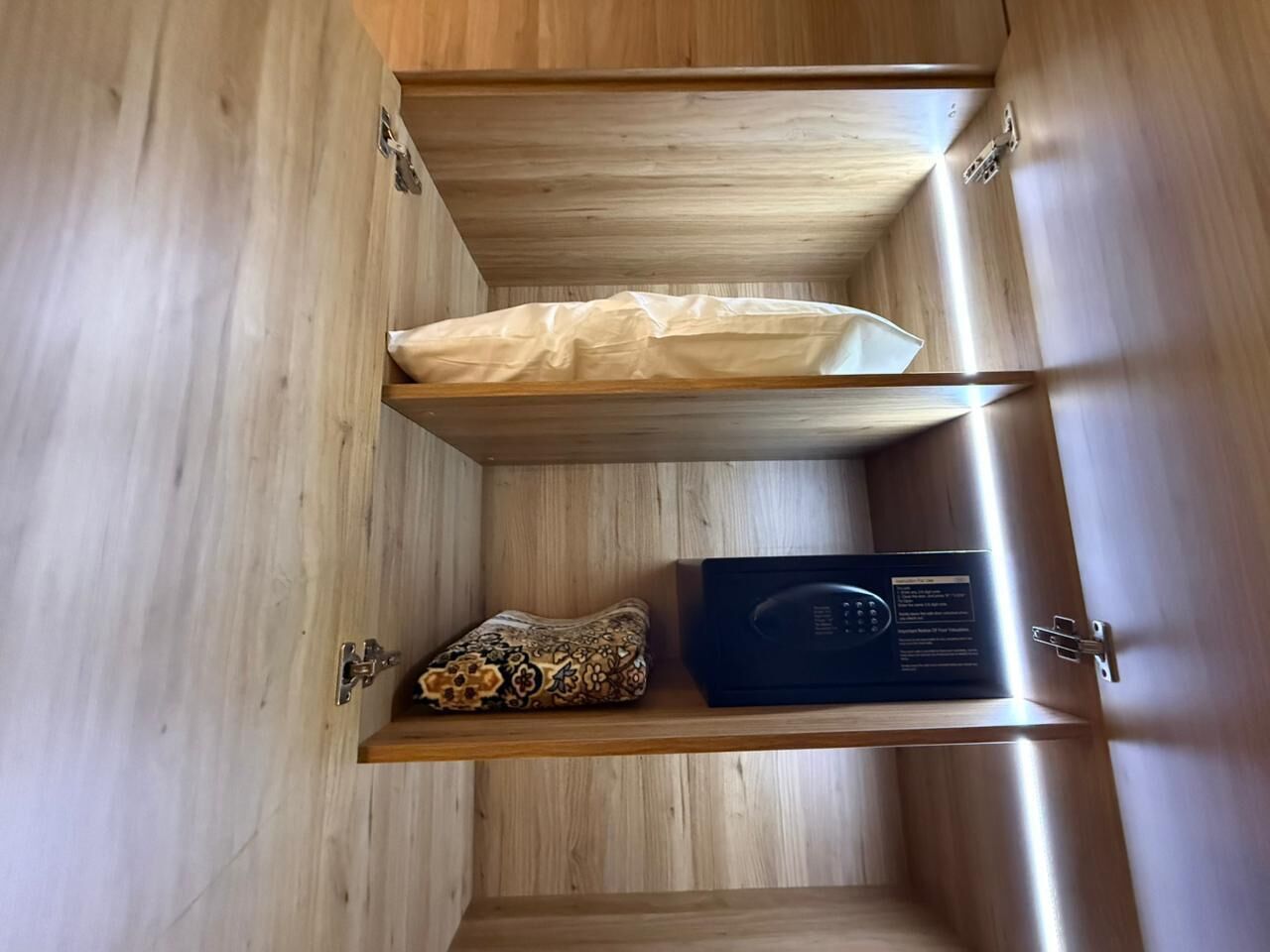 Un mueble de madera con un almohadón blanco, un cojín estampado y un dispositivo electrónico negro.