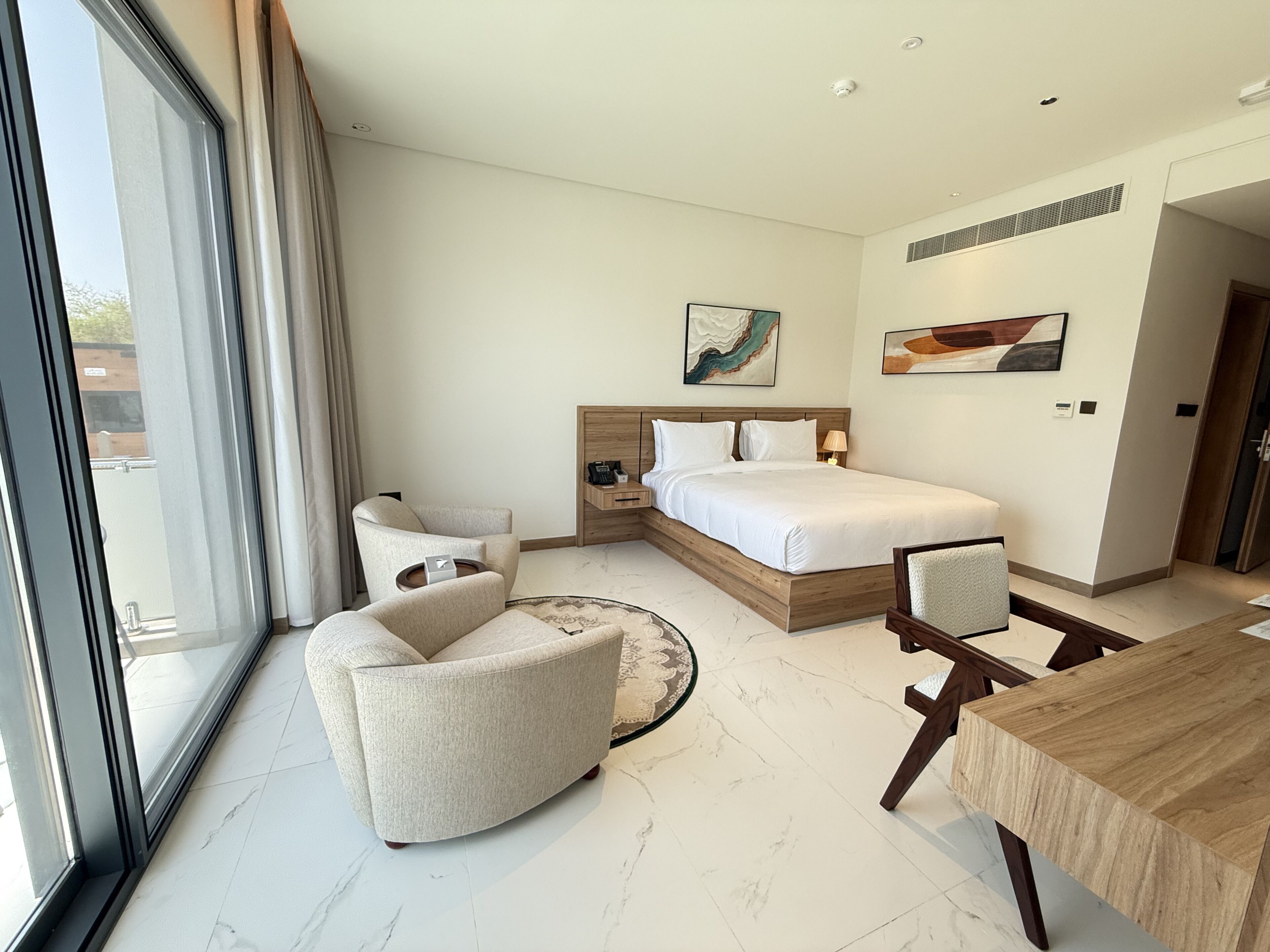 Habitación de hotel moderna con cama, escritorio, sillón, sofá y ventana grande.